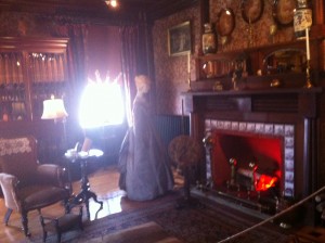 One of the rooms in Eldon House, with a fire place, a manequin dressed as a maid and many decorations on the wall. 